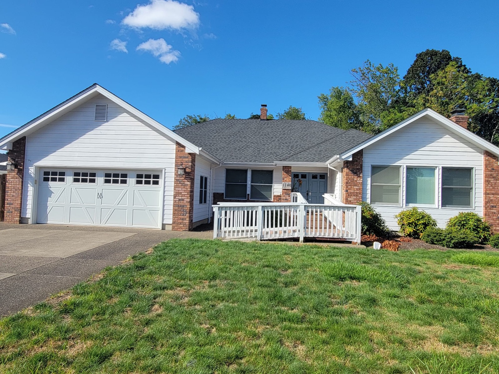 Angled view of the home showing the driveway, garage, front lawn and mature trees behind the house.